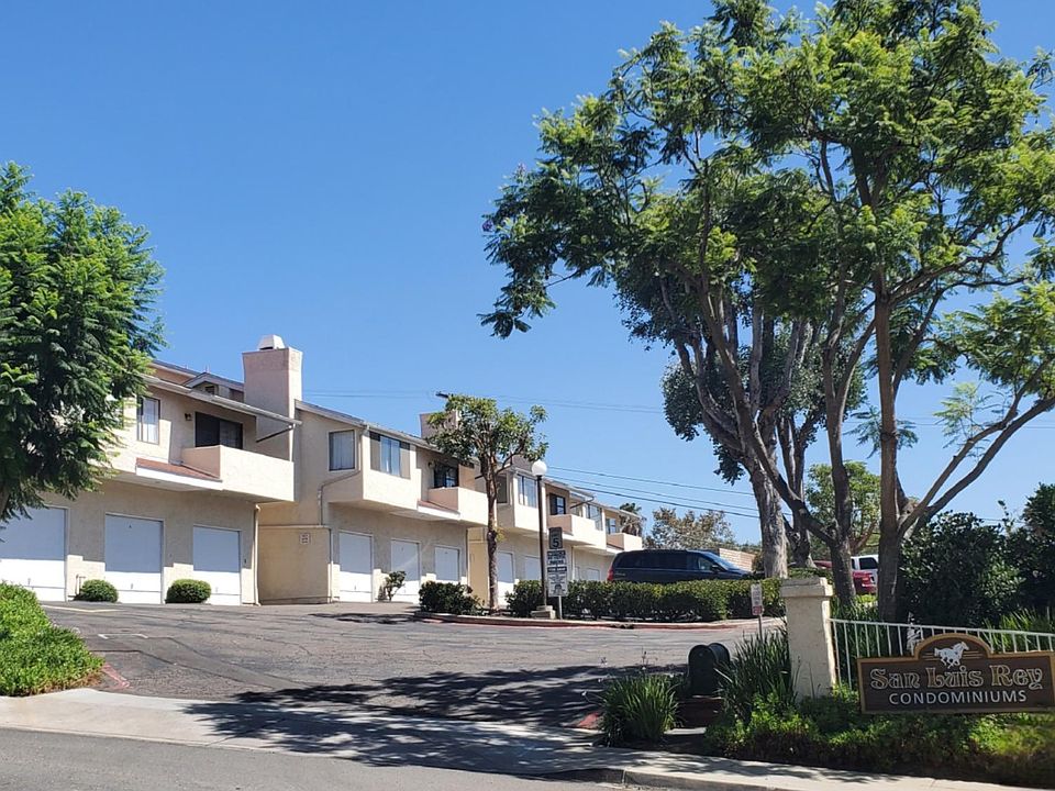 Front entrance view of complex shows off-street parking lot with private garages and assigned parking spaces for tenant use only.
