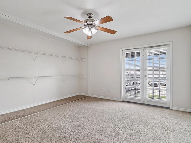 Elegant room with plush carpet, ceiling fan, and French doors leading to a balcony, complemented by ample shelving space. Elegant room with plush carpet, ceiling fan, and French doors leading to a balcony, complemented by ample shelving space.