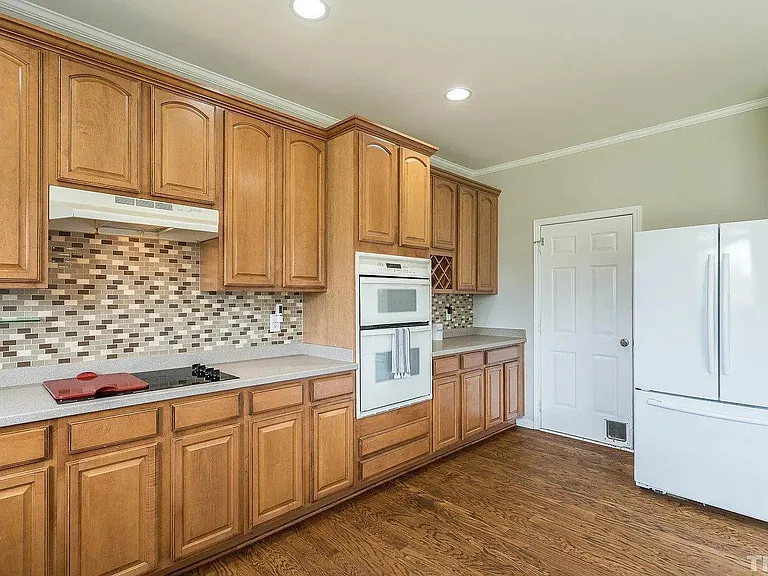 Kitchen with many cabinets, stove, microwave, oven, and refrigerator. Door leads to two car garage.