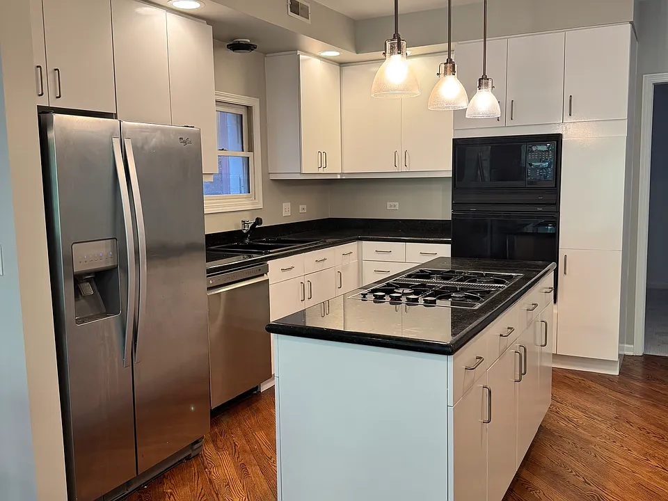 Gourmet kitchen featuring a center island with gas cooktop, dark granite countertops, and white cabinets.