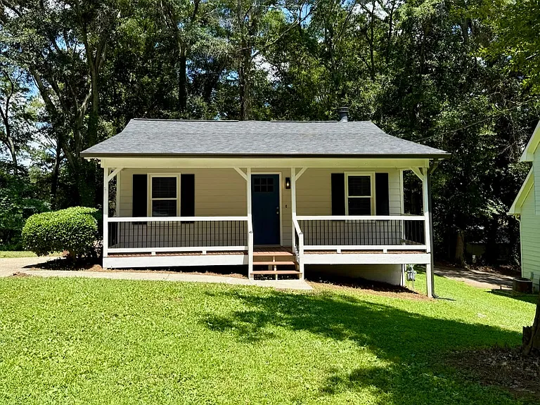 Charming covered front porch_ dark shutters boost curb appeal - lush green yard shaded by mature oaks invites weekend grilling or evening relaxation.
