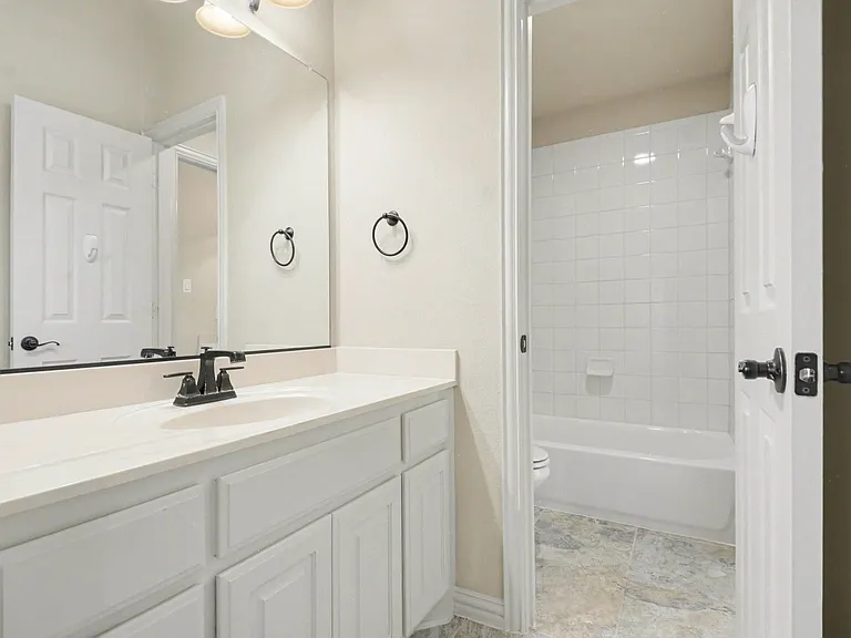 Bathroom featuring a white vanity with an integrated sink and matte black faucet, a large mirror, and a wall-mounted light fixture