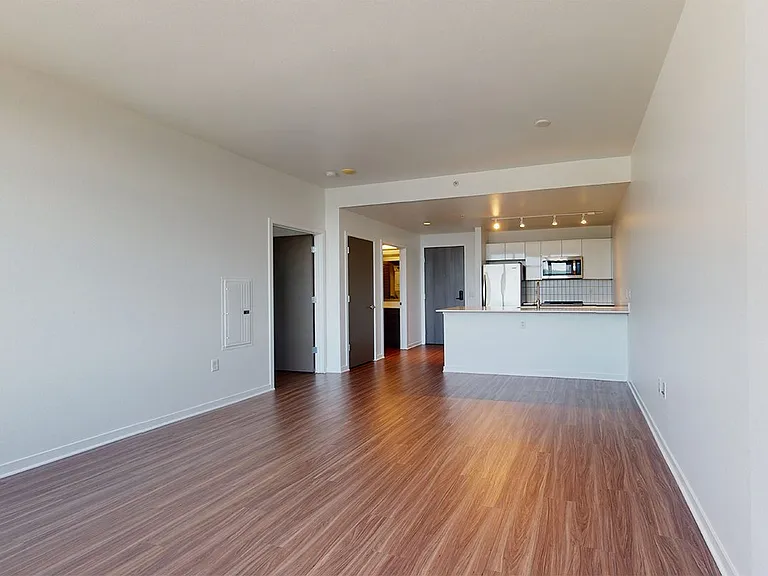 Apartment kitchen with stainless steel appliances, dining and living room with wood-style flooring.