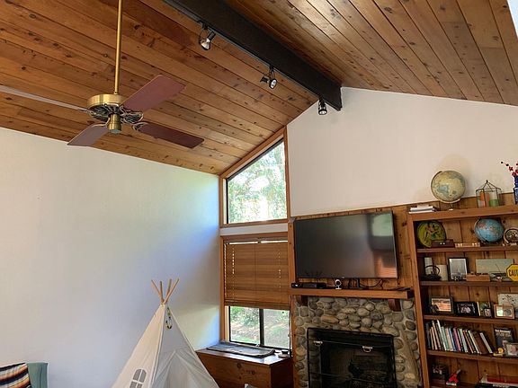 Living room with vaulted ceiling, ceiling fan, gas fireplace and built in cabinet/ bookshelf. Off screen is a dining area off the living room.
