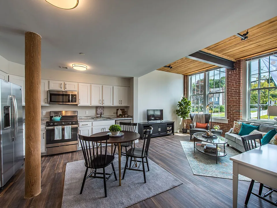View Of Living, Dining Room And Kitchen. Stainless Steel Appliances, Brick Wall, Large Windows.