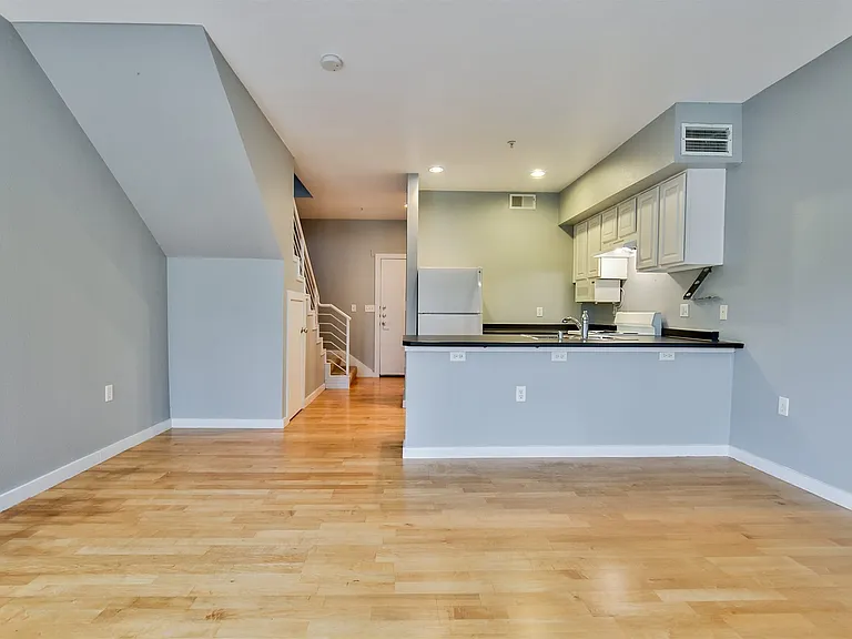 Open-concept living space featuring wood-finish flooring, a kitchen with white cabinetry, a built-in refrigerator, and a breakfast bar with a dark countertop