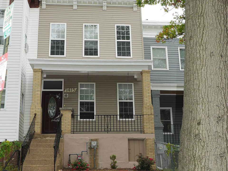 Handsome row house with decorative brick wall and pillars, wrought iron gate, and lovely front porch