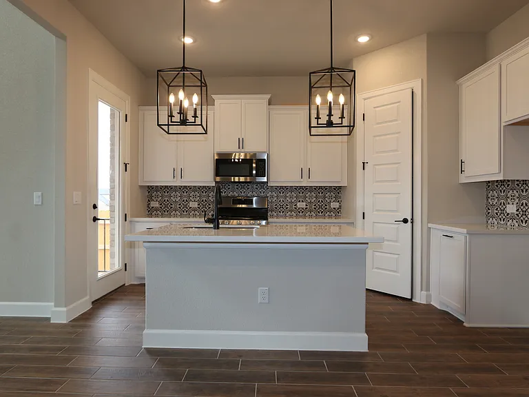 Bright white kitchen with stunning backsplash, brand-new appliances, elegant light fixtures, and abundant storage.