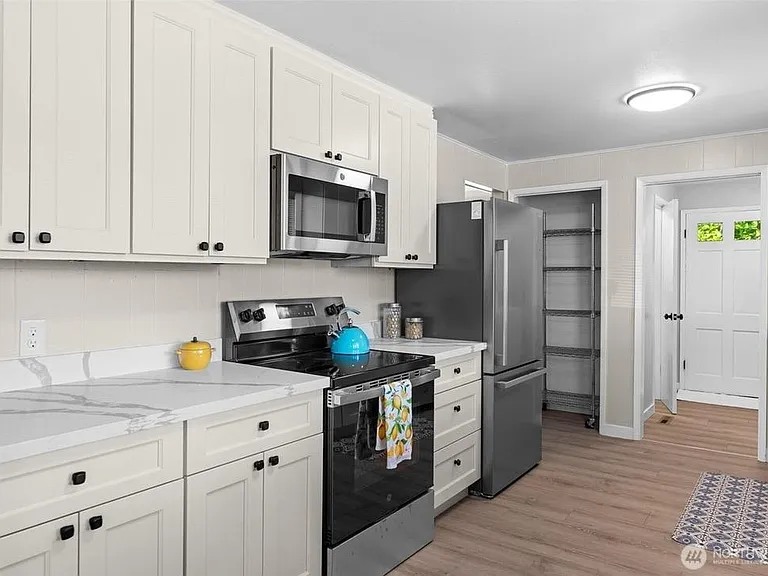 Efficient kitchen with ample white cabinetry, stone-look counters, and stainless appliances plus a walk-in pantry.