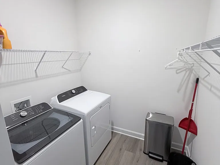 Dedicated laundry room with full-size washer and dryer, durable flooring, and wire shelving for convenient storage.