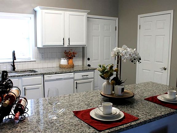 Kitchen - white cabinetry, appliances, granite countertop, kitchen bar, sink and access to patio.