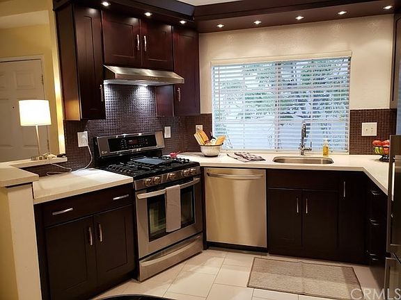 The kitchen has neutral tile flooring, tile backsplash and stainless steel appliances and sink