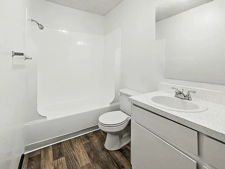Modern bathroom with sleek white fixtures, a spacious bathtub, elegant vanity, and beautiful wood-patterned flooring.