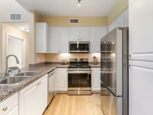 Renovated Package I kitchen with stainless steel appliances, beige speckled granite countertop, white cabinetry, and hard surface flooring - Avalon Glendale