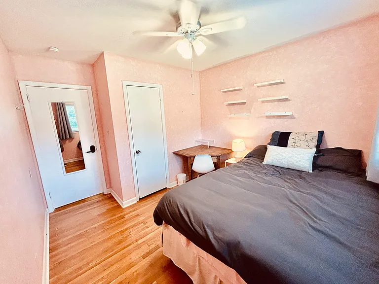Furnished bedroom with hardwood floors, ceiling fan, wall shelving, and a dedicated desk area near the window.