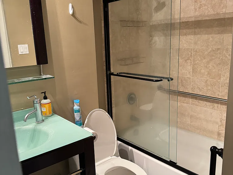 Full bath with modern vanity, glass-enclosed shower/tub combo, and tile flooring.