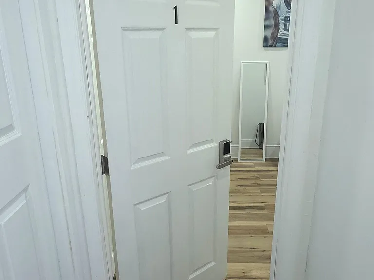 Clean hallway entry with wood-look flooring leading into a private room, featuring a keyed lock for added privacy.