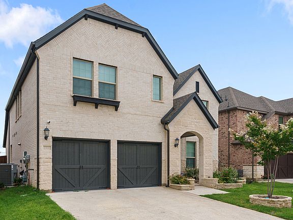 View of front of home with brick siding, driveway, two-car garage, and front lawn