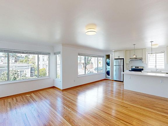 Spacious living room with a wood-like flooring, large windows, an in-unit washer and dryer, and a view of the kitchen
