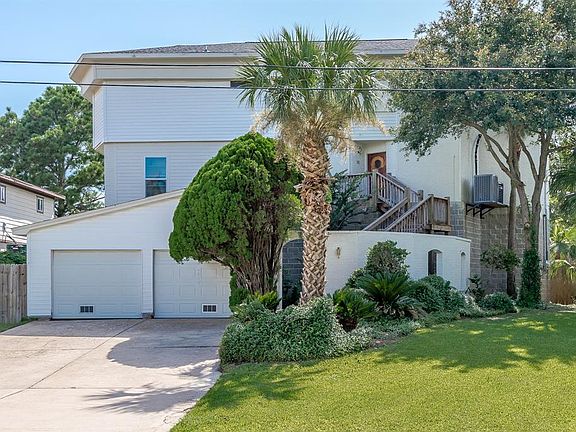 FRONT ELEVATION AT 146 SANDY CV. THE HOME FEATURES A 2 CAR GARAGE WITH A PULL THROUGH FOR A 3RD CAR OR GOLF CART. THE HOME SITS AT 21' ELEVATION WHICH IS EXTREMELY HIGH FOR THE AREA. FROM THE BALCONIES, YOU CAN LOOK ACROSS THE TREE TOPS TO CLEAR LAKE