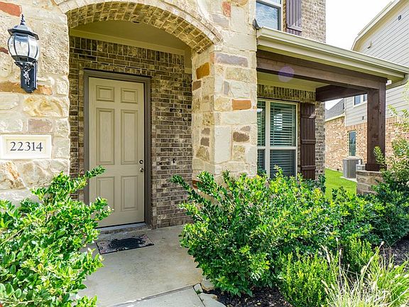 Charming brick and stone elevation with a covered front porch is adorned by lush landscaping and offers a place to sit and relax with a glass of iced tea.