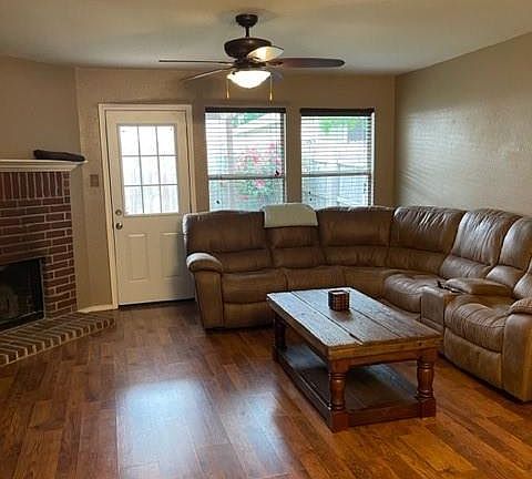 Living room featuring plenty of natural light, a ceiling fan, a brick fireplace, and wood finished floors