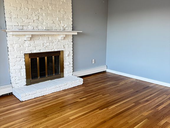 Living room featuring beautifully refinished hardwood floors and a painted white brick fireplace with mantel.