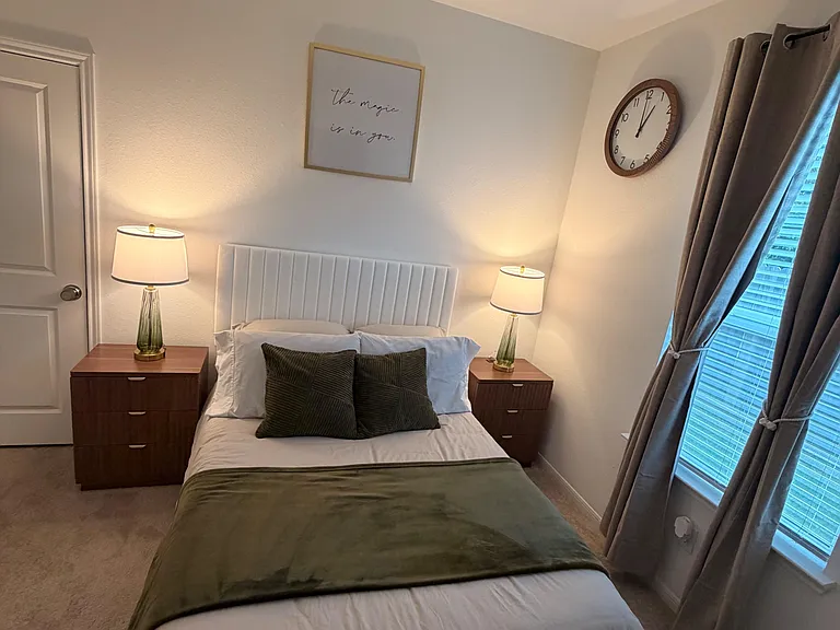 Well-appointed bedroom with a full bed, matching nightstands, and a large window with curtains and blinds.