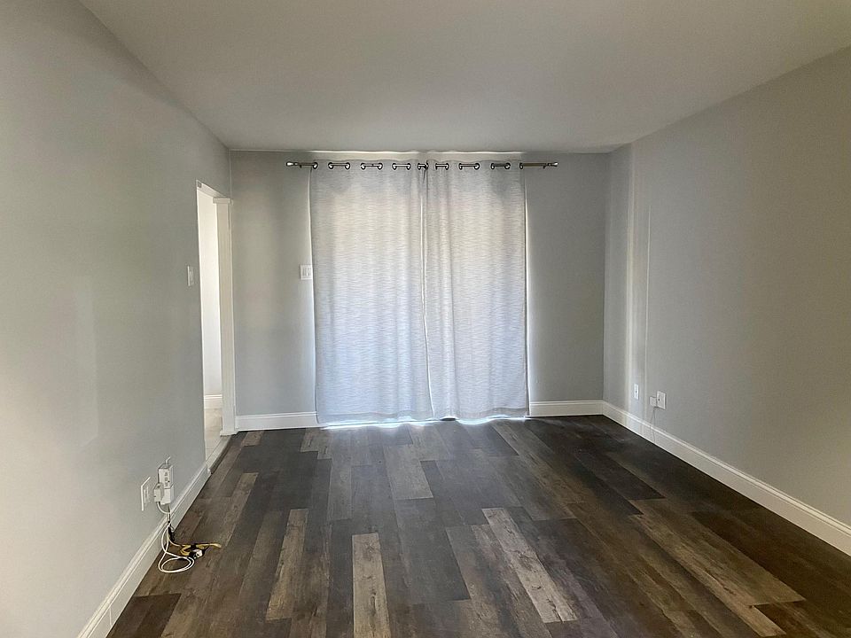 Large living area has plank flooring, great natural light, and neutral, warm grey wall paint.