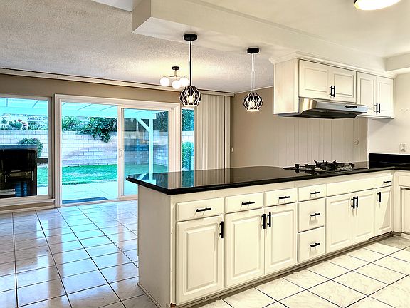 Large kitchen with gas cooktop, stainless steel appliances (fridge with water filter and ice maker), microwave, oven, dishwasher, large peninsula with overhang counter seating, opens to dining room and slider door leading to backyard.