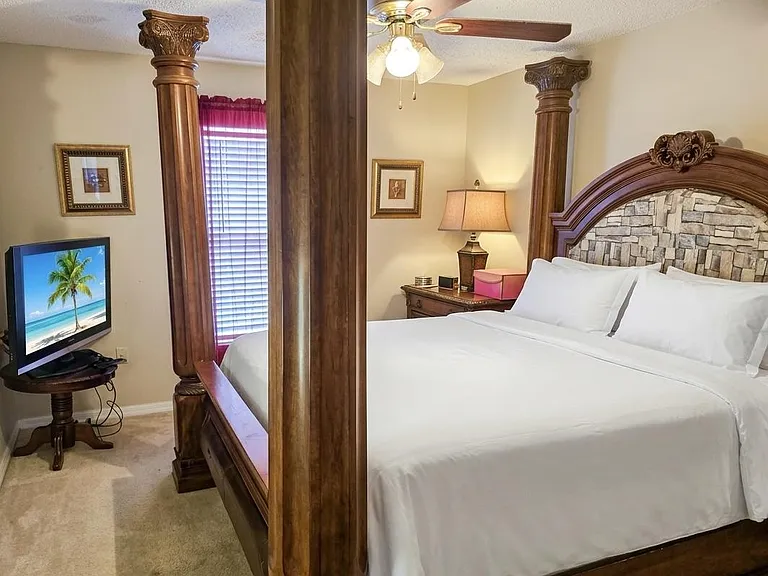 Primary bedroom with a four-poster bed, ceiling fan, nightstand lighting, and a window with blinds for privacy.
