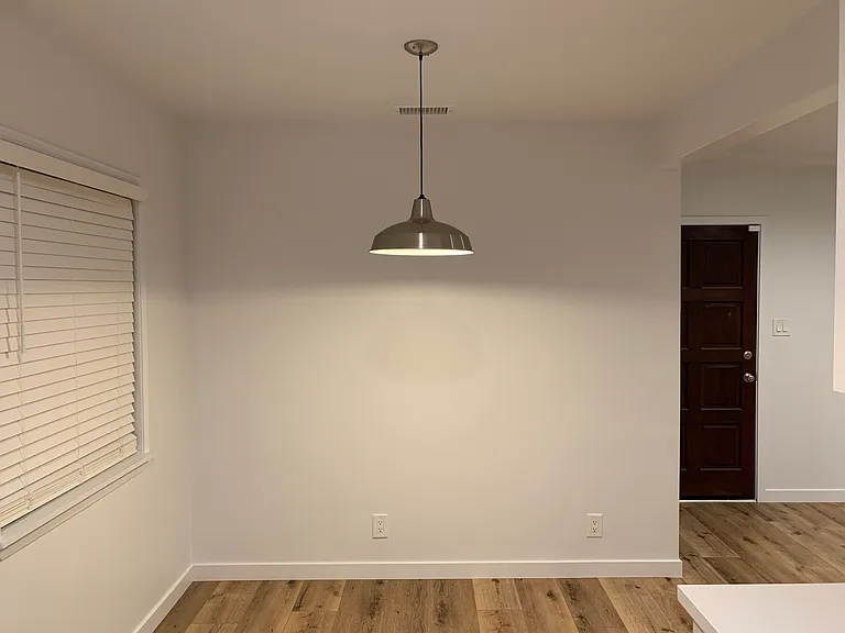 Dinning area featuring a modern pendant light, smooth walls and wood flooring, offering a clean and versatile space for everyday meals or entertaining.