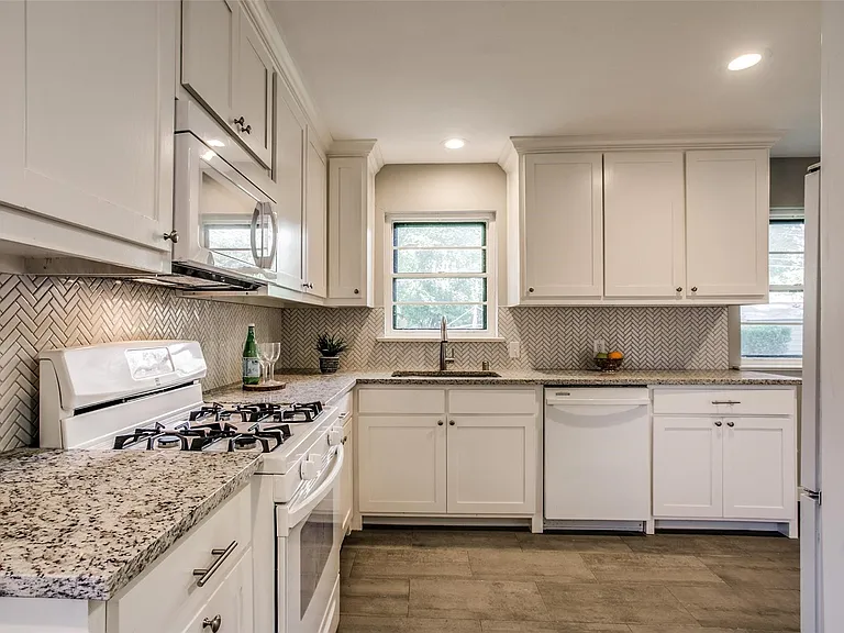 Kitchen featuring white cabinetry, granite countertops, a herringbone tile backsplash, stainless steel microwave, and wood-finish flooring