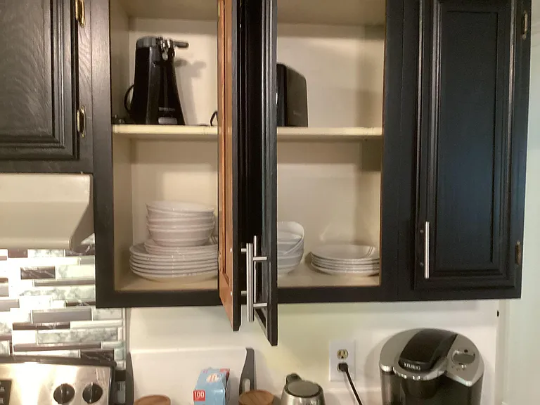 Kitchen storage cabinetry with open shelving for dishes and small appliances, set above a tiled backsplash and countertop.