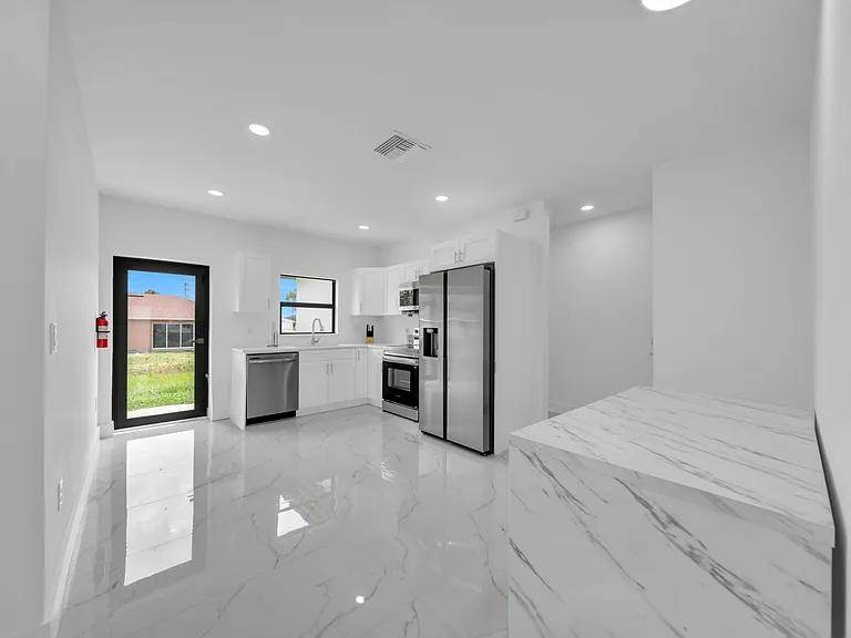Open kitchen with white cabinetry, stainless steel appliances, and a large waterfall island plus direct access to the yard.