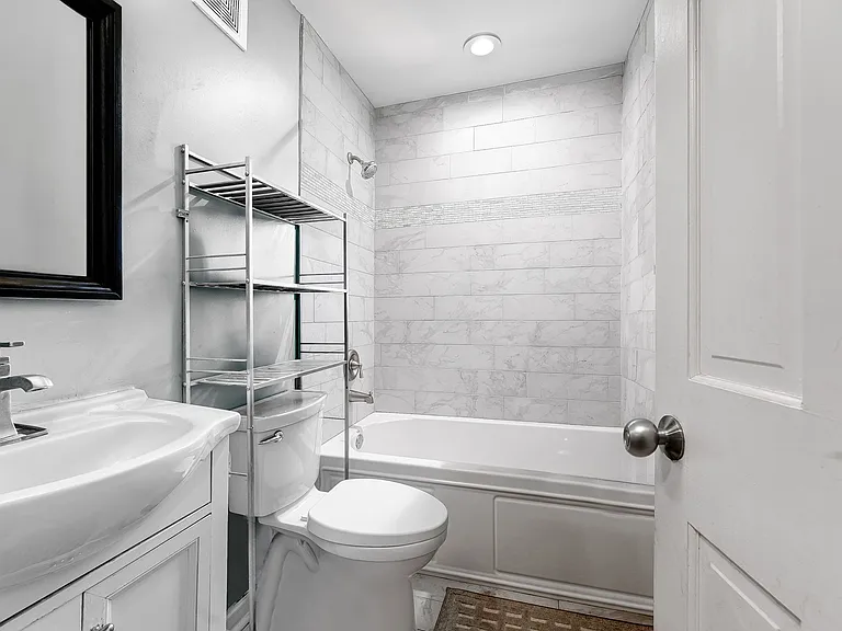 Main level first full bathroom with deep tub and shower, mirror, vanity and extra storage over toilet.