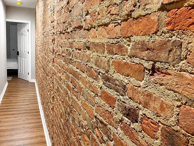 Hallway with exposed brick accent wall, recessed lighting, and wood-look flooring connecting to adjacent rooms.