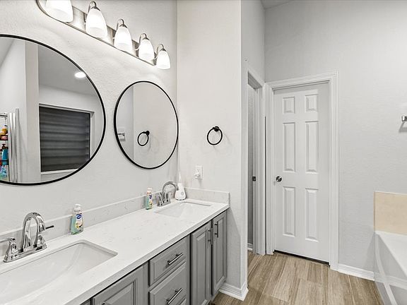 This bathroom features a modern design with dual sinks, stylish round mirrors, and a sleek vanity with ample storage. It includes contemporary fixtures, bright lighting, and a separate bathtub, offering both functionality and elegance.