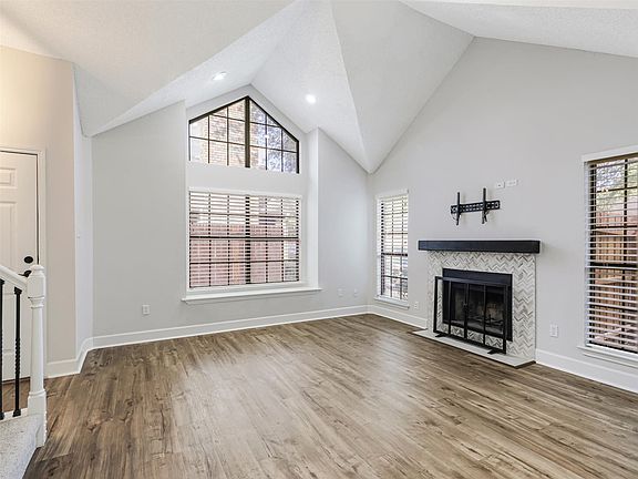Vaulted ceilings featuring recessed lighting, expansive triangular accent window, fireplace with herringbone tile surround and wood-finish mantel, and wood-finish flooring