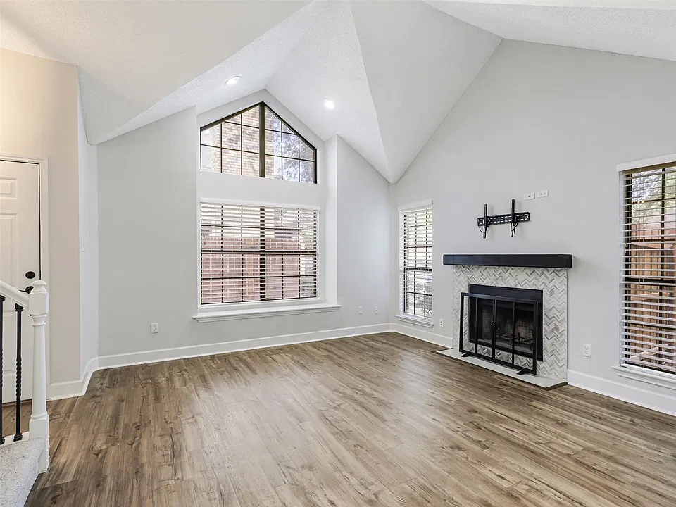 Vaulted ceilings featuring recessed lighting, expansive triangular accent window, fireplace with herringbone tile surround and wood-finish mantel, and wood-finish flooring