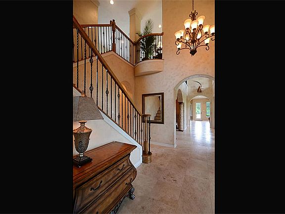 Guests enter the home from the covered front Porch into the Foyer that impresses with a 2-story ceiling completed with a massive chandelier, a wrought iron stair, travertine floors and a view of the stunning 2-story Gallery