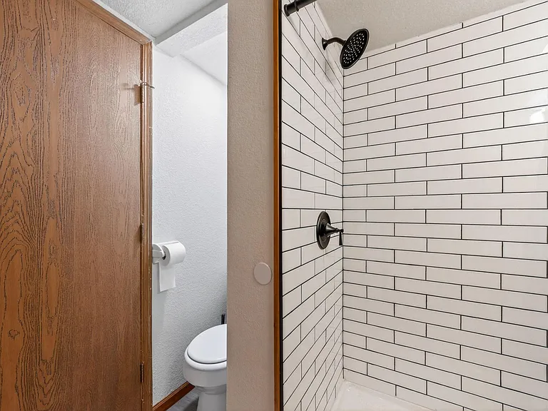 Bathroom features a tiled shower with dark fixtures and a convenient layout with toilet nearby for easy daily use.