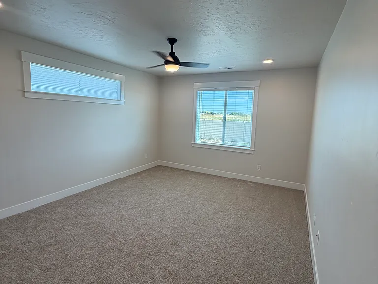 Retreat to the expansive primary bedroom, featuring large east- and south-facing windows that flood the room with warm natural light. The generous layout provides plenty of space for a sitting area or workspace.