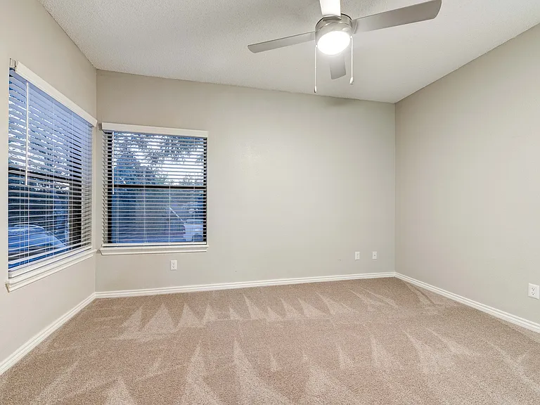 Spacious bedroom with plush carpeting and large windows showcasing serene views, complemented by a sleek ceiling fan for optimal comfort.