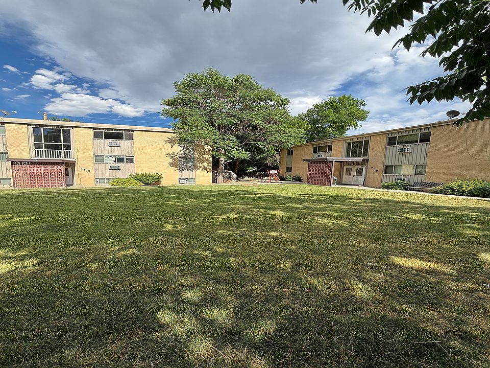 Charming apartment complex with brick exterior and lush green courtyard under a vibrant blue sky.