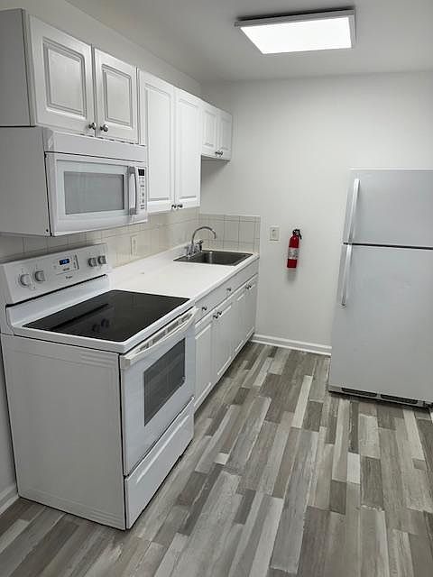 Kitchen with white cabinets, full size stove, fridge and microwave. New grey laminate flooring.