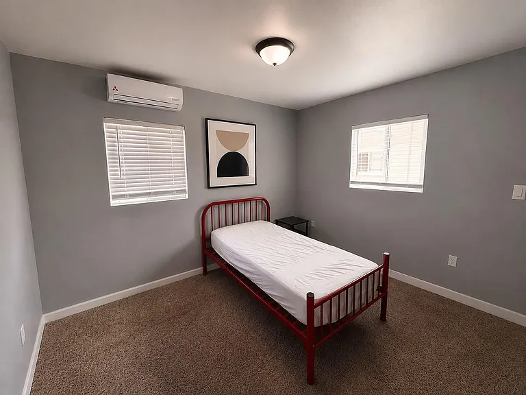 Private bedroom with two windows, neutral paint, carpeted floors, and a wall-mounted mini-split for added comfort.