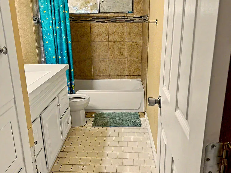 Full bathroom with tiled tub/shower surround, vanity storage, and a shower curtain for added privacy.