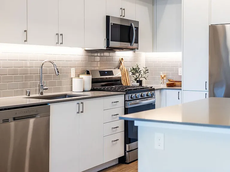 Kitchen with grey quartz countertops, white cabinetry, grey subway tile backsplash, stainless steel appliances, and hard surface flooring