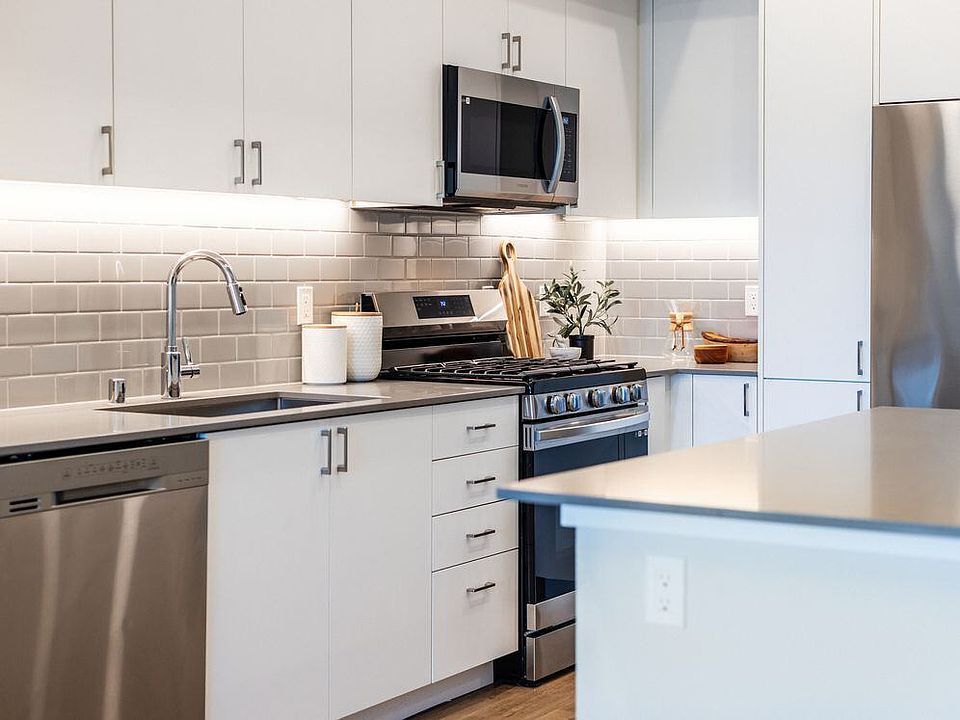 Kitchen with grey quartz countertops, white cabinetry, grey subway tile backsplash, stainless steel appliances, and hard surface flooring